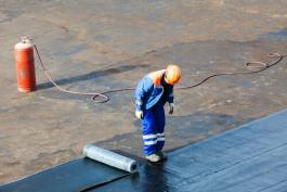 פועל בניין במהלך איטום גג עם יריעות של מבנה גדול באופקים